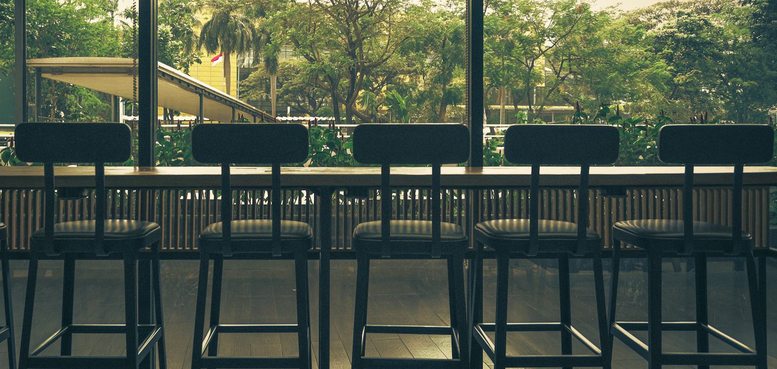 A row of bar stools facing a window onto green trees